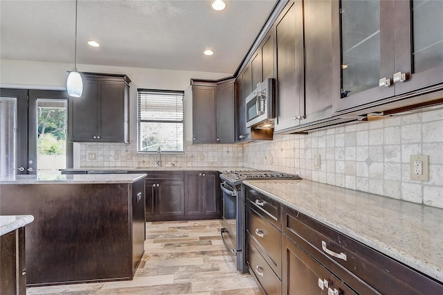 kitchen with light stone countertops, stainless steel appliances, sink, and decorative light fixtures