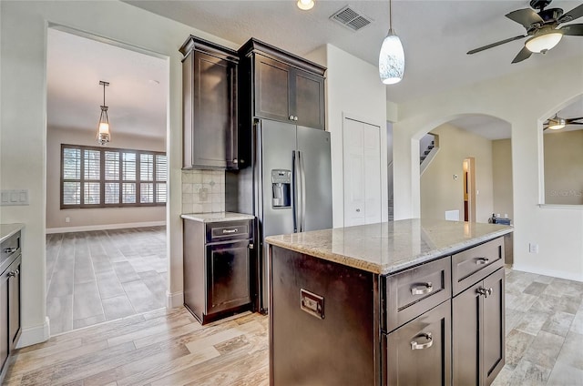 kitchen featuring decorative light fixtures, backsplash, a center island, stainless steel fridge, and dark brown cabinets