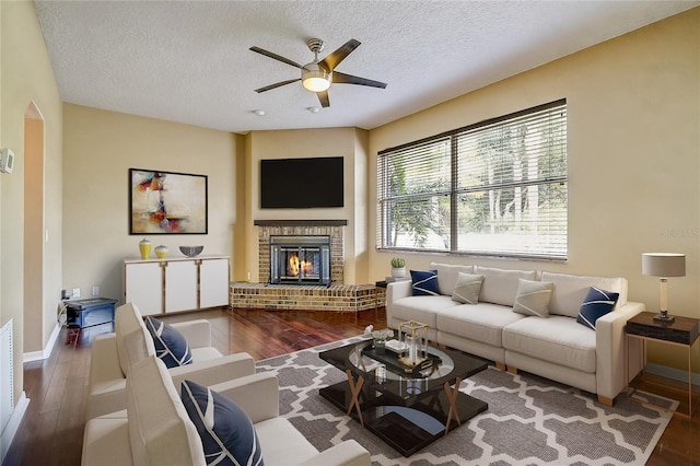 living room with a textured ceiling, ceiling fan, a fireplace, and wood-type flooring