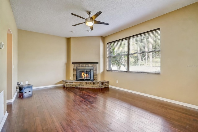 unfurnished living room with a brick fireplace, a textured ceiling, hardwood / wood-style flooring, and ceiling fan