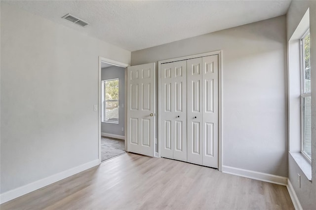 unfurnished bedroom featuring light hardwood / wood-style floors, a textured ceiling, and a closet