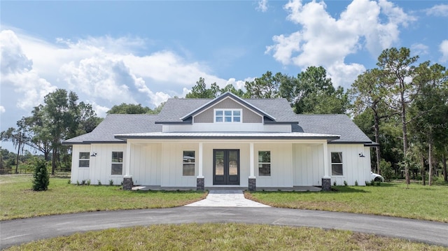 modern farmhouse featuring covered porch, french doors, board and batten siding, and a front yard