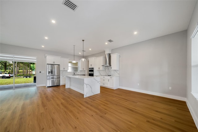 kitchen with tasteful backsplash, wall chimney range hood, a kitchen island, white cabinetry, and appliances with stainless steel finishes