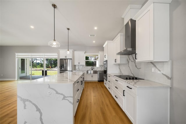 kitchen featuring decorative light fixtures, wall chimney range hood, a kitchen island, stainless steel appliances, and white cabinets