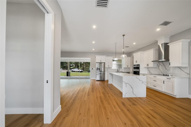 kitchen featuring white cabinets, a center island, wall chimney exhaust hood, decorative light fixtures, and stainless steel appliances