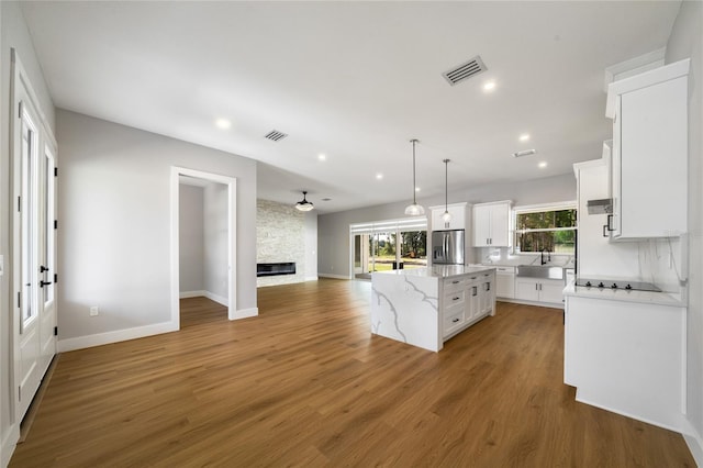 kitchen featuring a kitchen island, stainless steel refrigerator with ice dispenser, hardwood / wood-style flooring, hanging light fixtures, and white cabinets