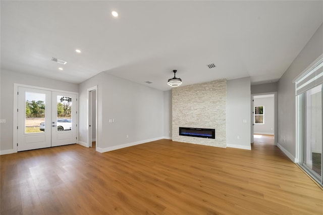 unfurnished living room featuring french doors, a stone fireplace, and light wood-type flooring