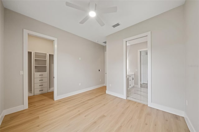 unfurnished bedroom featuring ceiling fan, ensuite bathroom, light hardwood / wood-style floors, a spacious closet, and a closet