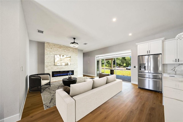 living room featuring dark wood-style floors, visible vents, a fireplace, and baseboards