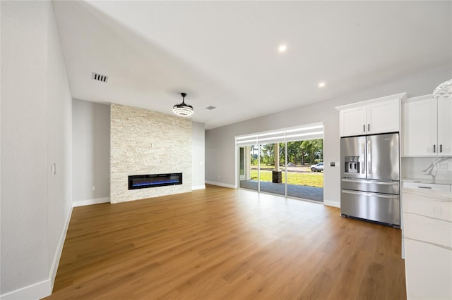 unfurnished living room with visible vents, a ceiling fan, a stone fireplace, wood finished floors, and baseboards