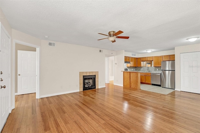 unfurnished living room with a tile fireplace, a textured ceiling, light wood-type flooring, and ceiling fan