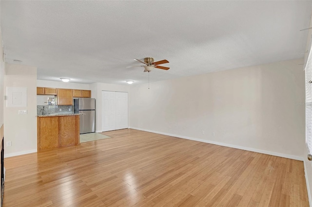 unfurnished living room featuring ceiling fan, a textured ceiling, light wood-type flooring, and baseboards