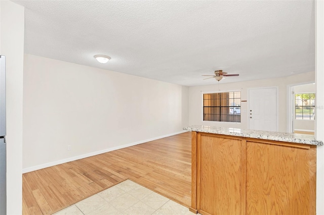 kitchen featuring light wood-style floors, a ceiling fan, open floor plan, a textured ceiling, and baseboards