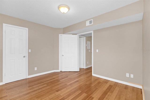 empty room with light wood finished floors, visible vents, and baseboards