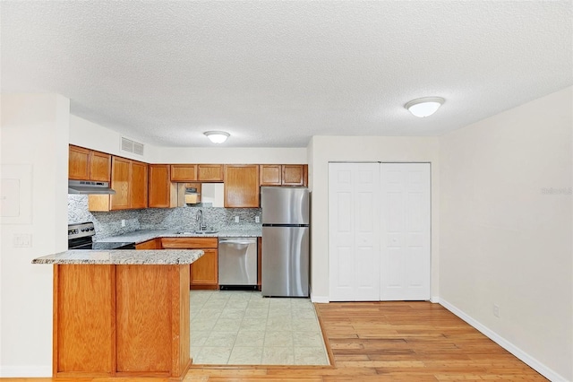 kitchen with brown cabinets, visible vents, backsplash, appliances with stainless steel finishes, and under cabinet range hood