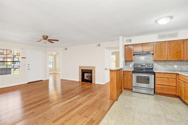 kitchen with tasteful backsplash, visible vents, a tile fireplace, under cabinet range hood, and stainless steel range with electric stovetop