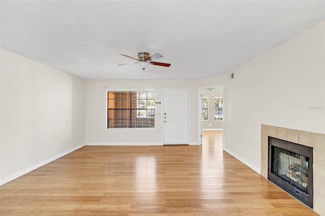 unfurnished living room with ceiling fan, a textured ceiling, light wood-type flooring, baseboards, and a tile fireplace