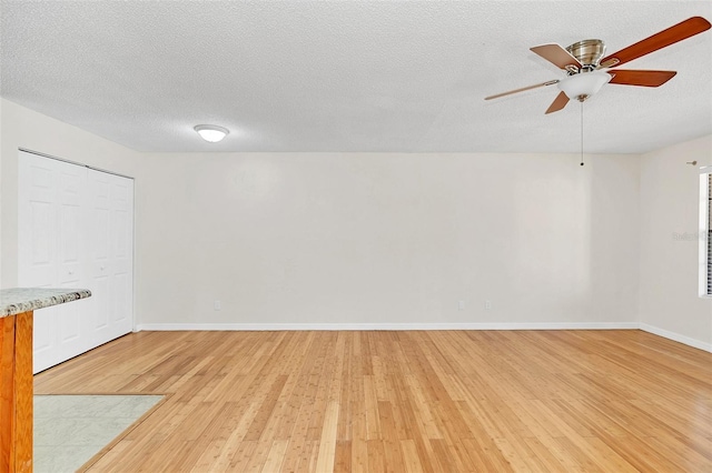 spare room featuring a ceiling fan, baseboards, light wood-style flooring, and a textured ceiling