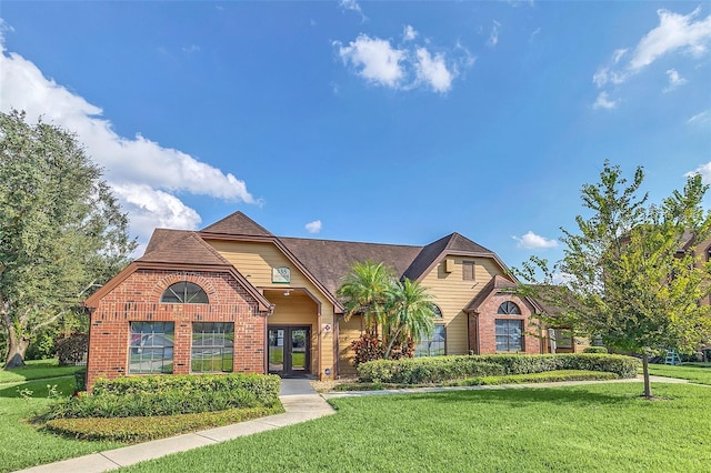 view of front of home with french doors, brick siding, and a front lawn