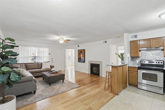 living room featuring light wood-type flooring, visible vents, a ceiling fan, and a tile fireplace