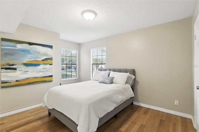 bedroom with a textured ceiling, wood finished floors, and baseboards