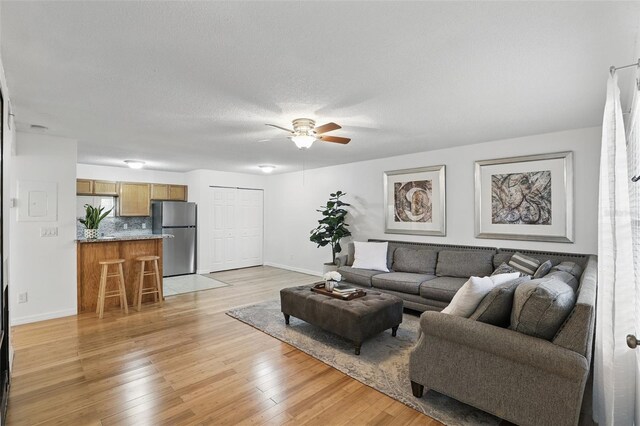 living room with a textured ceiling, light wood-type flooring, a ceiling fan, and baseboards