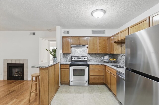 kitchen with stainless steel appliances, a peninsula, visible vents, and under cabinet range hood