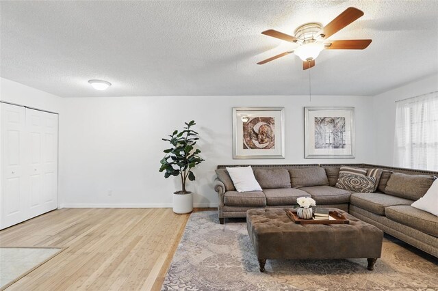 living area featuring light wood-style floors, ceiling fan, a textured ceiling, and baseboards