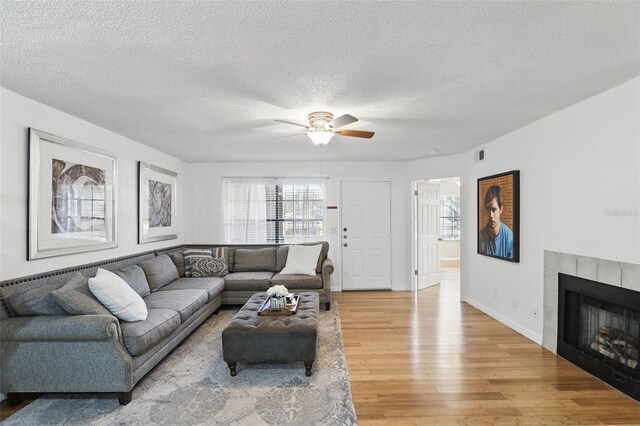 living room featuring a fireplace, light wood finished floors, visible vents, a ceiling fan, and baseboards