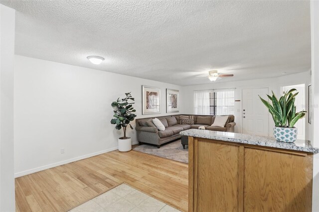 living room featuring a textured ceiling, light wood finished floors, a ceiling fan, and baseboards