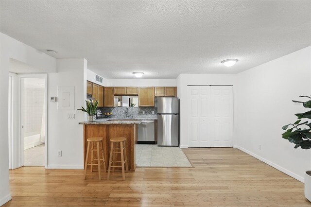 kitchen featuring light wood finished floors, visible vents, brown cabinetry, a peninsula, and stainless steel appliances