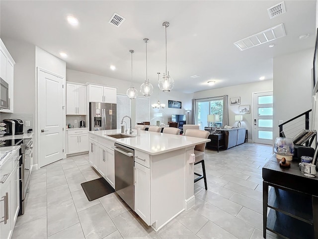 kitchen featuring sink, white cabinetry, a center island with sink, pendant lighting, and stainless steel appliances