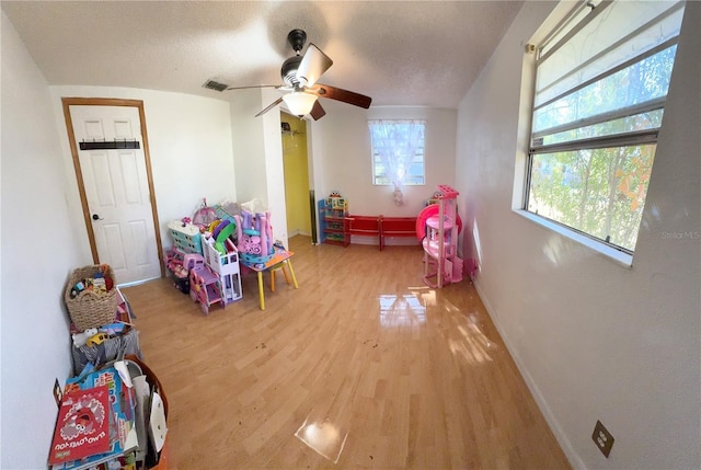 playroom featuring a textured ceiling, ceiling fan, and light hardwood / wood-style flooring