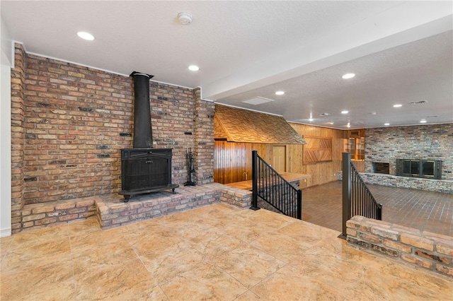 unfurnished living room with a textured ceiling, wooden walls, and brick wall