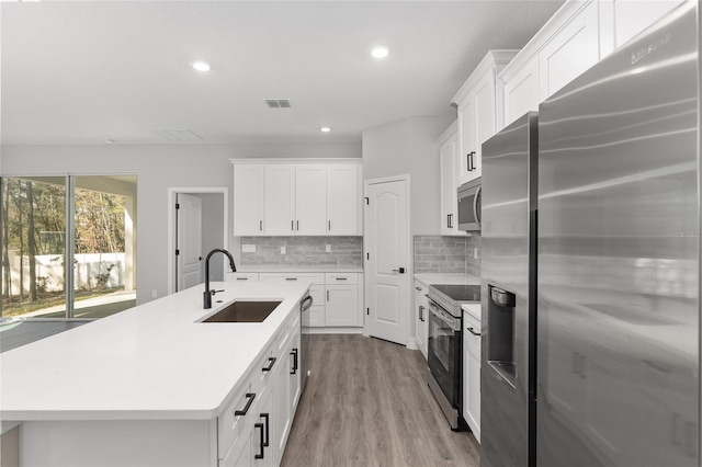 kitchen with stainless steel appliances, sink, white cabinets, tasteful backsplash, and a center island with sink