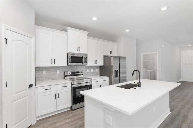 kitchen with stainless steel appliances, white cabinetry, an island with sink, and sink