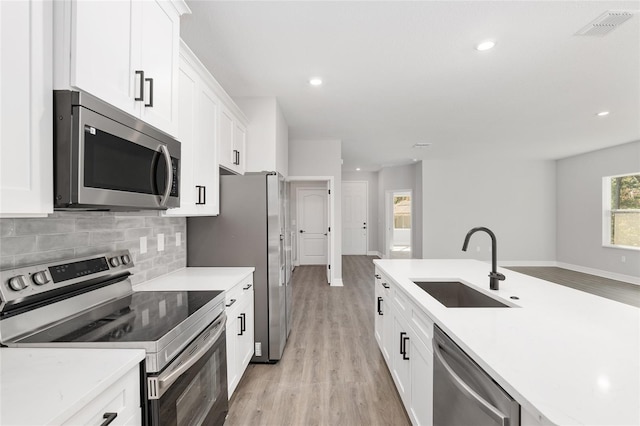 kitchen with appliances with stainless steel finishes, light hardwood / wood-style floors, sink, white cabinetry, and tasteful backsplash