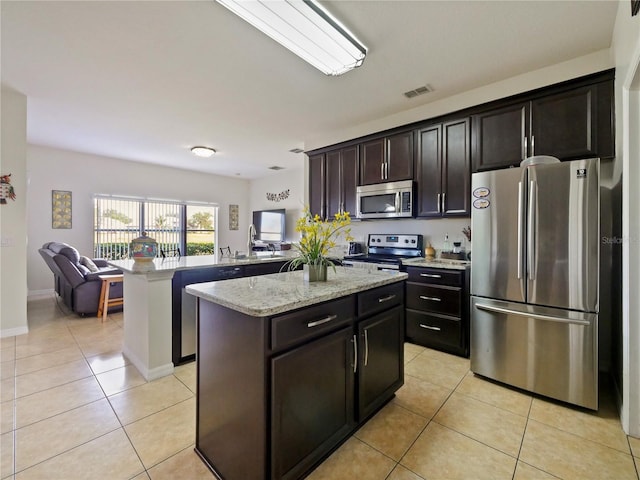 kitchen featuring appliances with stainless steel finishes, a center island, kitchen peninsula, light tile patterned floors, and dark brown cabinetry