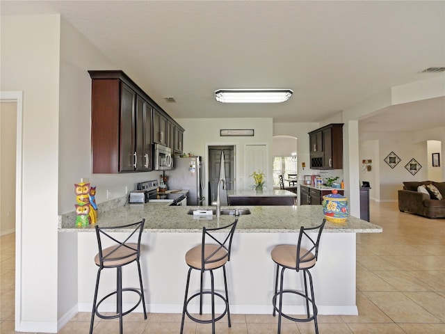 kitchen with stainless steel appliances, sink, light tile patterned floors, kitchen peninsula, and light stone countertops