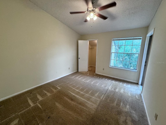 unfurnished bedroom with ceiling fan, a walk in closet, a textured ceiling, and carpet flooring