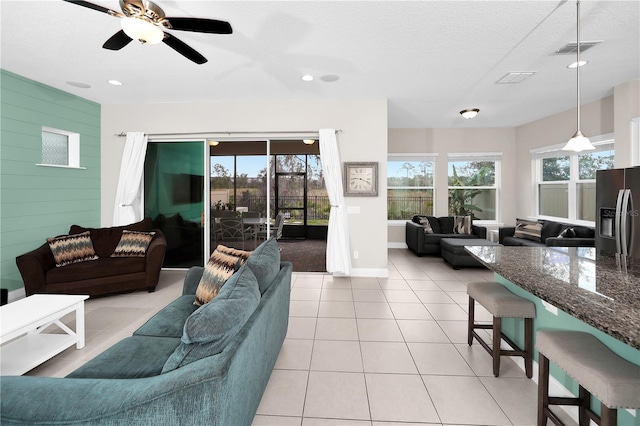 living room with ceiling fan, a textured ceiling, light tile patterned floors, and wood walls