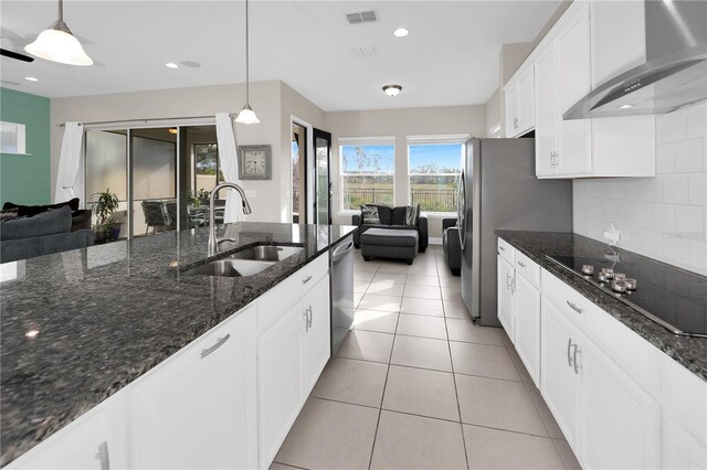 kitchen with pendant lighting, sink, appliances with stainless steel finishes, wall chimney exhaust hood, and dark stone counters