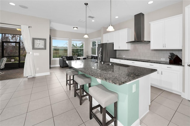 kitchen with stainless steel fridge, a center island with sink, a kitchen breakfast bar, wall chimney range hood, and white cabinets