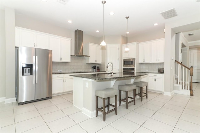 kitchen featuring a center island with sink, wall chimney exhaust hood, appliances with stainless steel finishes, white cabinetry, and light tile patterned flooring