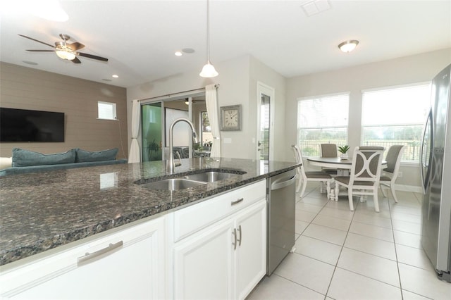 kitchen with stainless steel appliances, a sink, white cabinets, dark stone counters, and pendant lighting