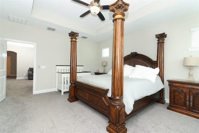 bedroom featuring arched walkways, a tray ceiling, visible vents, and light carpet