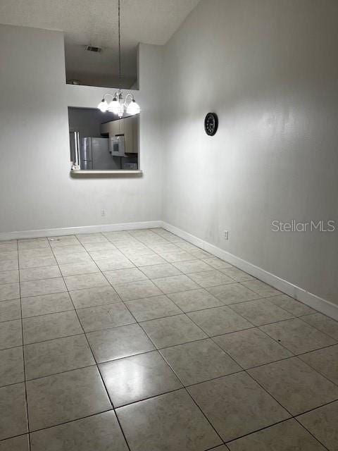 tiled spare room with lofted ceiling and a notable chandelier