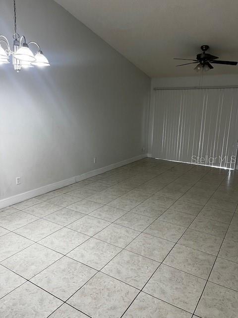 tiled empty room with ceiling fan with notable chandelier