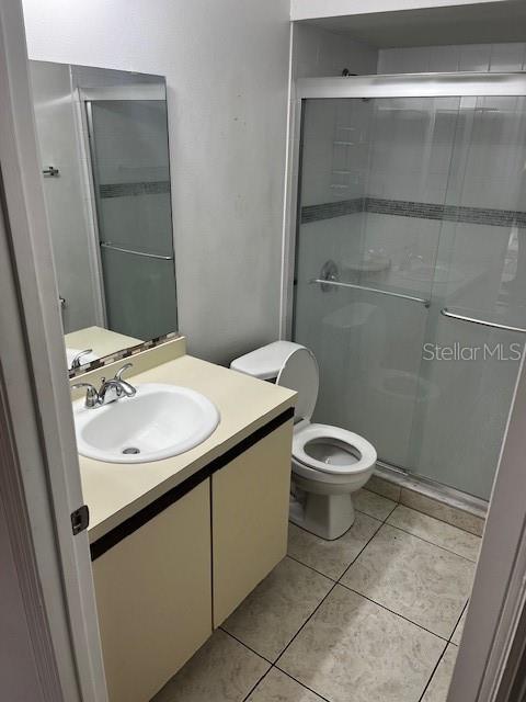 bathroom featuring vanity, toilet, walk in shower, and tile patterned flooring