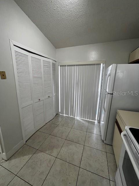 kitchen featuring light tile patterned floors, a textured ceiling, white appliances, and vaulted ceiling